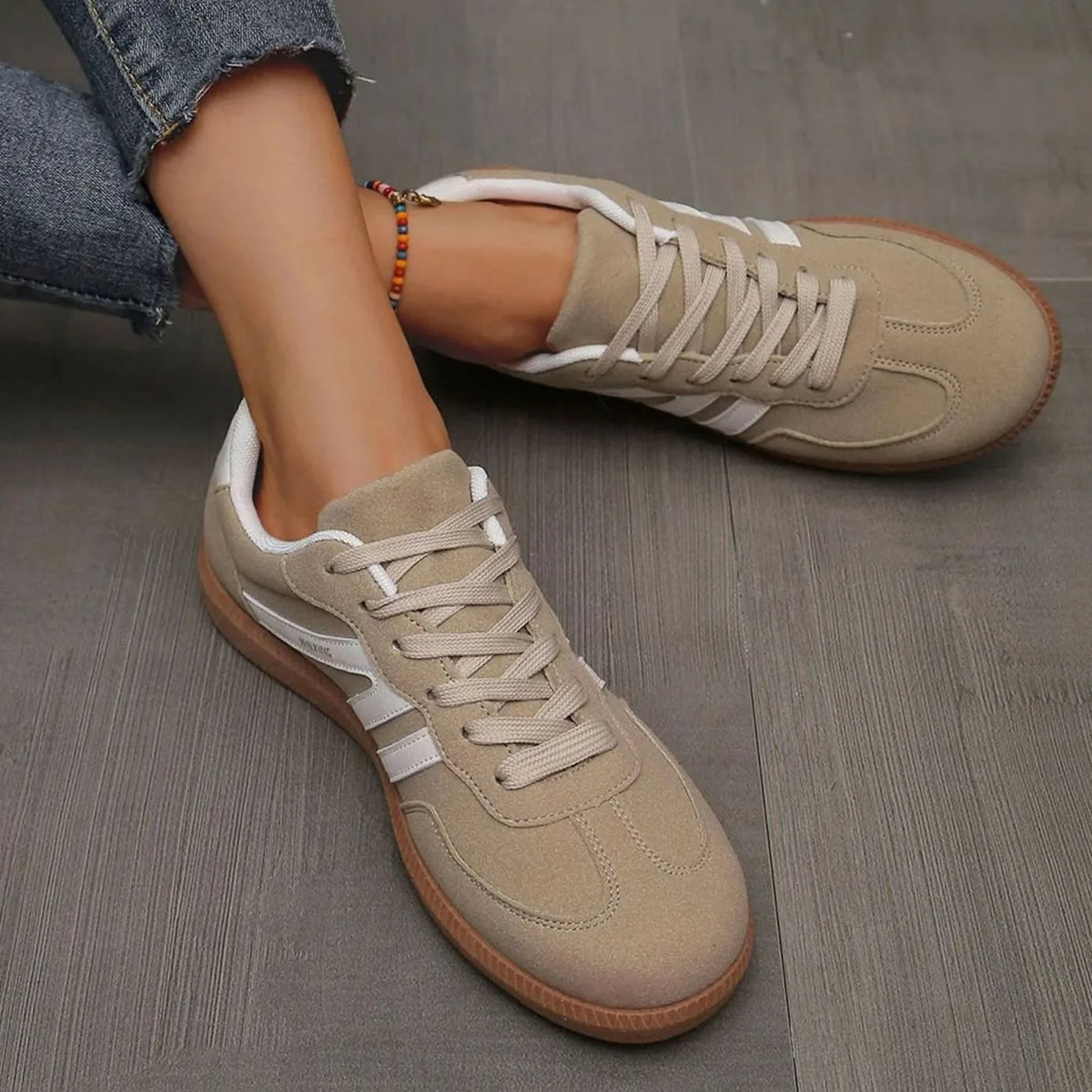 Beige trainers on foot from above, showing lace pattern and padded tongue with logo text
