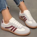 Brown suede trainers with tan stripes worn on foot, front angle on textured floor
