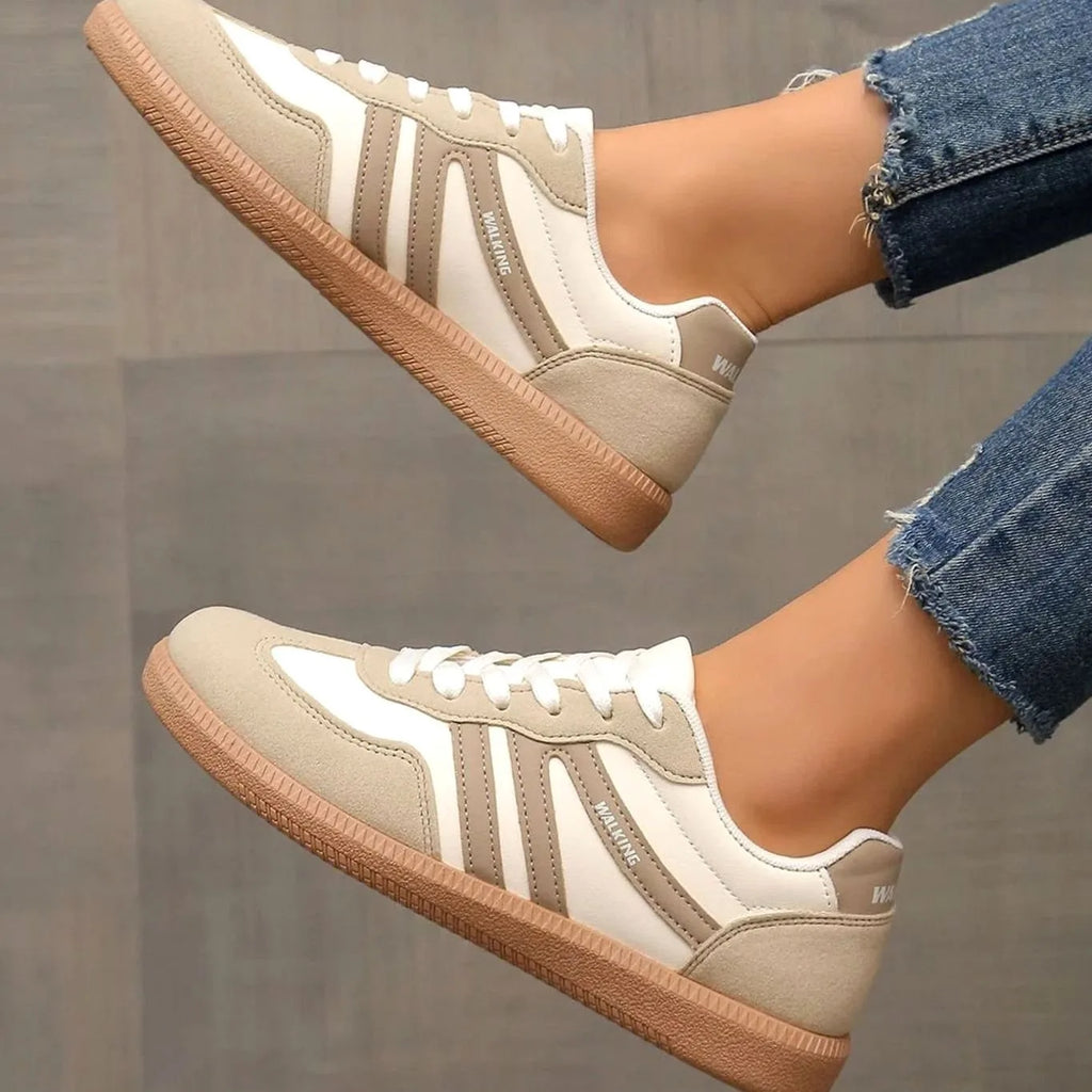 Side profile of beige trainers mid-step, highlighting curved stripe design and lace-up front