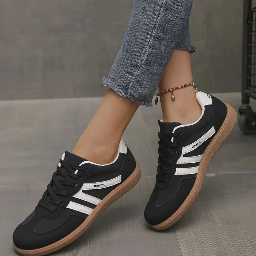 Side view of black trainers with white stripes and gum sole, foot lifted mid-stride