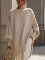 Woman wearing a beige oversized cashmere jumper with wide batwing sleeves and a soft crew neckline, holding a tan handbag