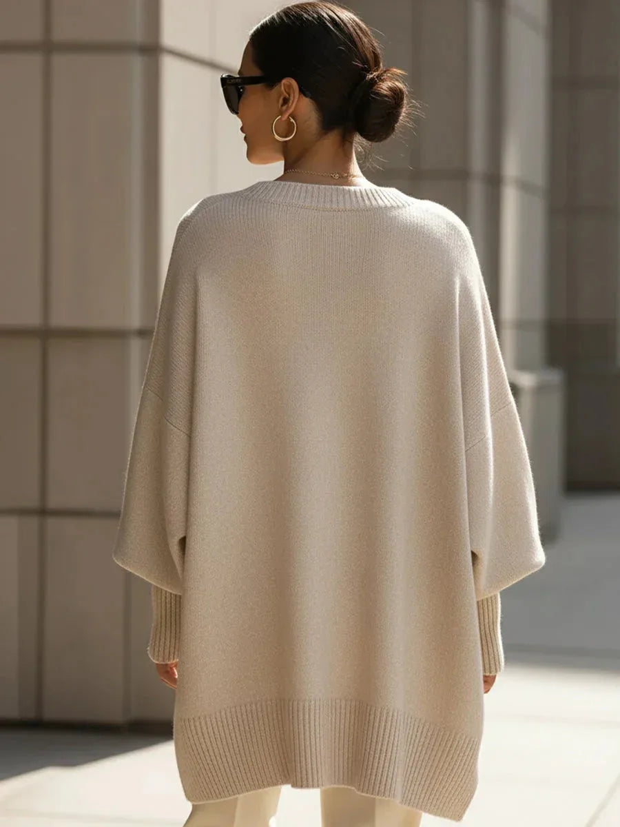 Back view of a woman in the beige jumper showing its cape-like drape and relaxed oversized fit