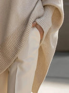 Close-up of a hand resting in the side pocket slit of the beige jumper with ribbed cuff detail visible