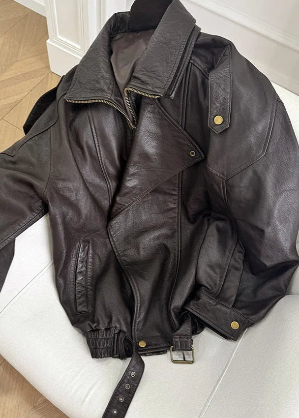 Close-up of the unbuttoned brown leather jacket laid flat, showing the buckle belt and interior lining