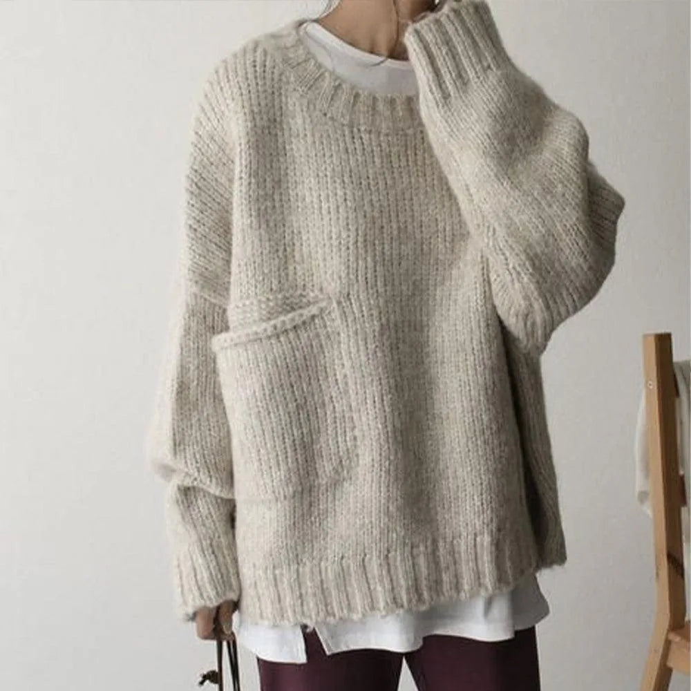 Front view of an oversized beige chunky knit jumper with ribbed crew neckline and a patch pocket on the hip, worn over a white tee