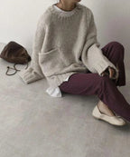 Seated model wearing the beige ribbed jumper with ballet flats, brown pouch bag and burgundy trousers underneath