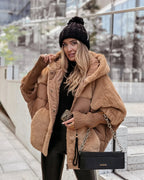 Woman wearing a camel oversized puffer coat with faux fur trim, hood up, carrying a black chain shoulder bag