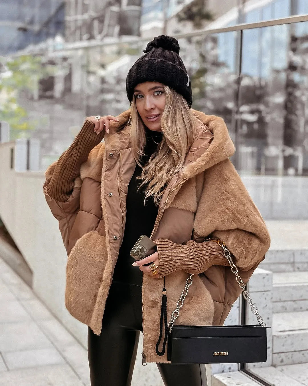 Woman wearing a camel oversized puffer coat with faux fur trim, hood up, carrying a black chain shoulder bag