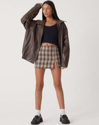 Front view of the brown oversized leather jacket worn open with a plaid mini skirt and chunky black loafers