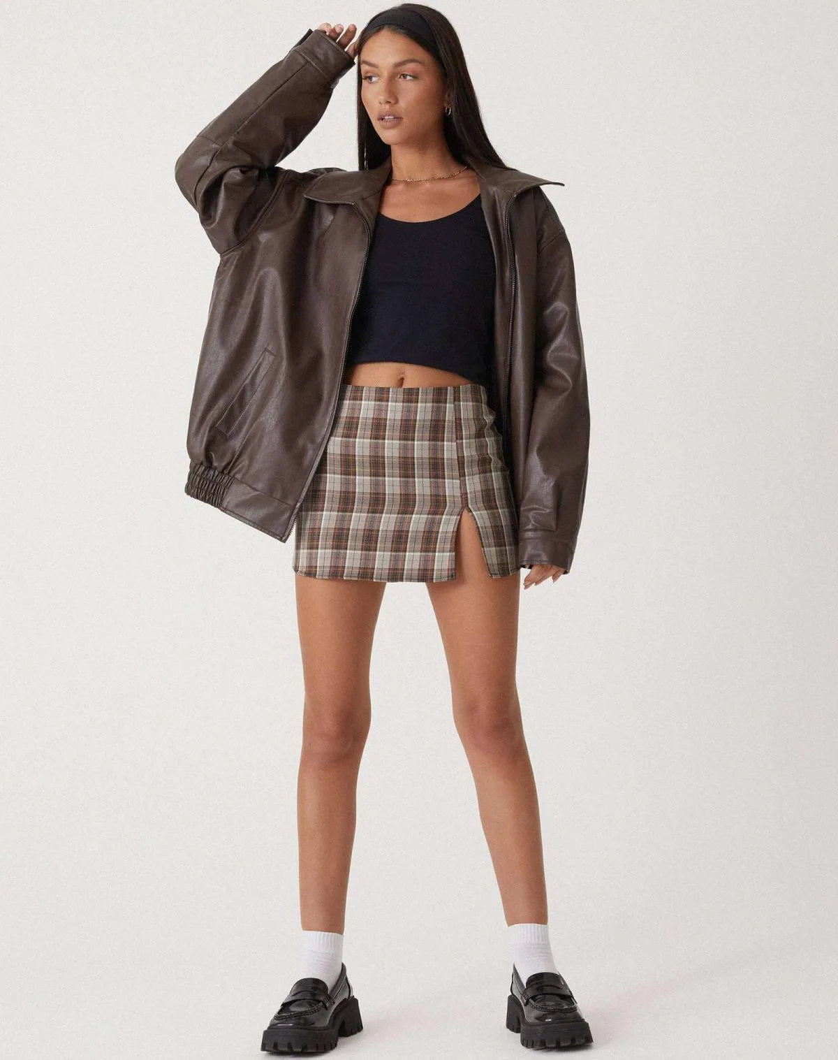 Front view of the brown oversized leather jacket worn open with a plaid mini skirt and chunky black loafers