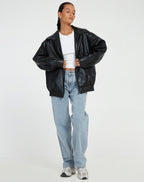 Model wears a black oversized faux leather jacket open over a white top with light wash straight jeans