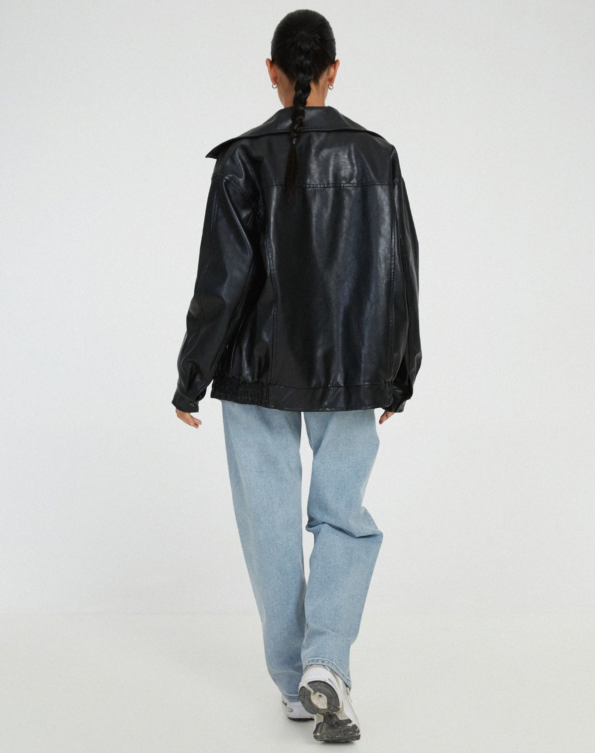 Back view of the black oversized leather jacket worn with a braided hairstyle and light denim