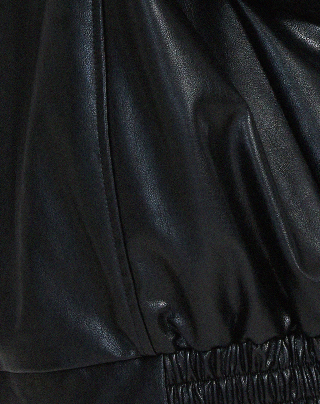 Three-quarter back view of the black leather jacket showing sleeve volume and overall relaxed silhouette