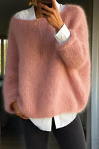 Close-up of a woman wearing an oversized dusty pink mohair-style jumper layered over a white shirt with black trousers