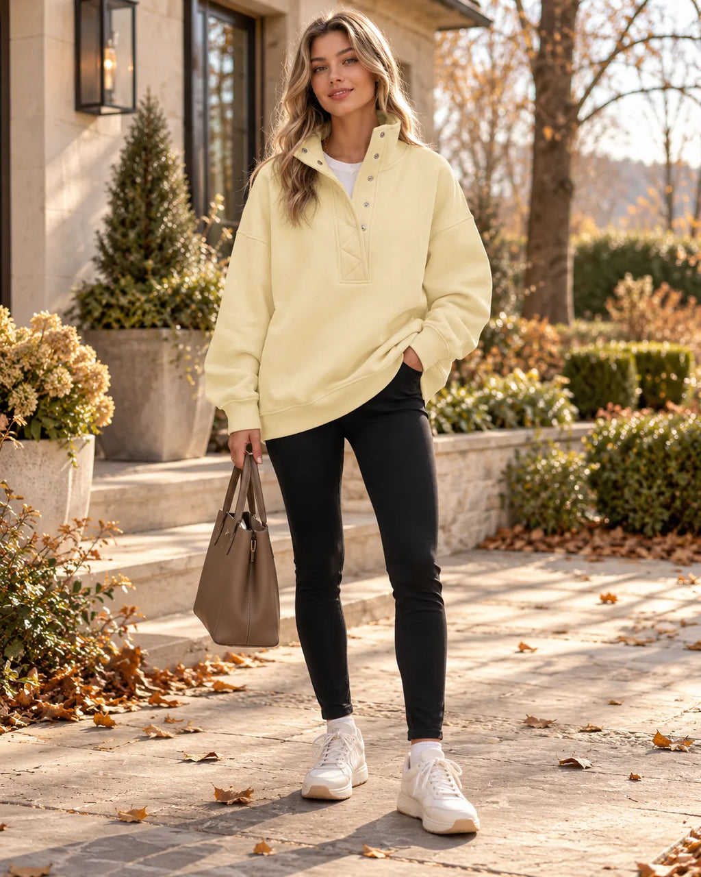 Pale yellow oversized henley sweatshirt with ribbed cuffs and hem, worn with black leggings and white trainers on a stone pathway.