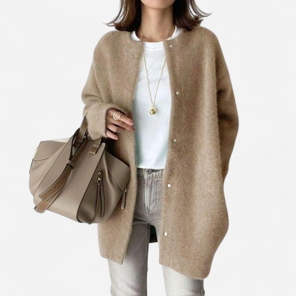 Woman wearing an oversized camel knit cardigan with snap-button fastening, over a white top and jeans, holding a taupe tote bag.
