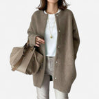 Close-up front view of a taupe brown oversized cardigan with snap buttons, worn over a white top and grey jeans.