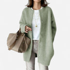 Sage green knit cardigan with round collar and snap fastenings, styled with a white top, jeans and a tote bag.