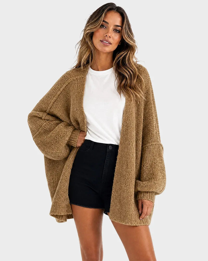 Woman wearing an oversized camel knit cardigan with lantern sleeves over a white tee and black shorts, front view