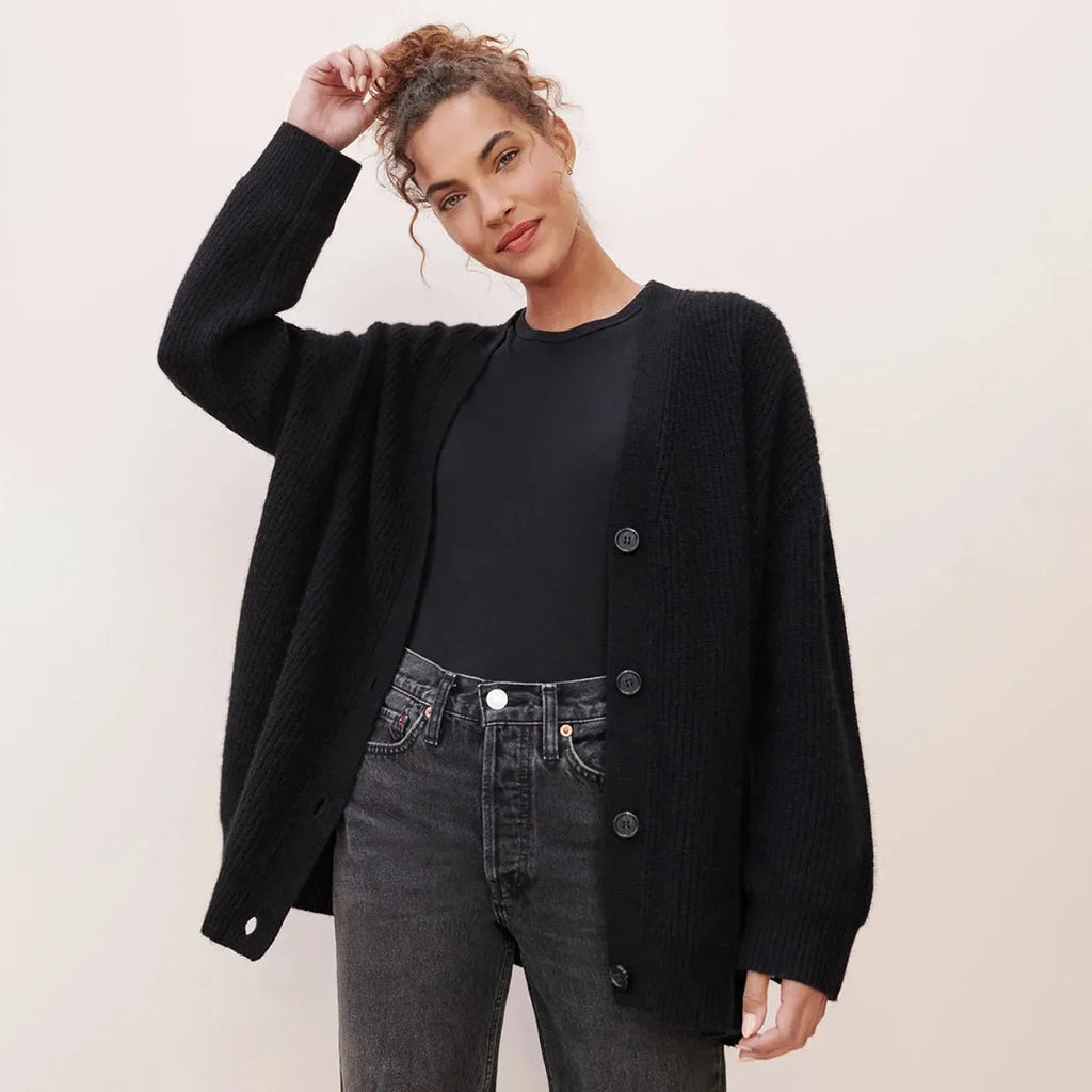 Close front view of a woman in an unbuttoned black ribbed cardigan over a black top and dark jeans