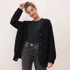 Close front view of a woman in an unbuttoned black ribbed cardigan over a black top and dark jeans