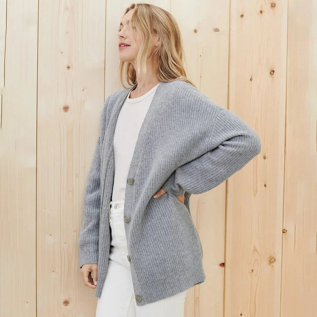 Side view of a woman wearing an open grey ribbed cardigan over a white t-shirt and white trousers