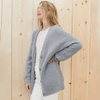 Side view of a woman wearing an open grey ribbed cardigan over a white t-shirt and white trousers
