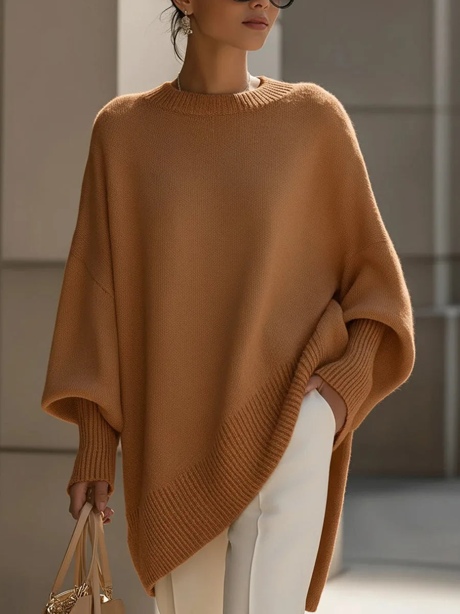 Model wearing a camel knit jumper with asymmetric ribbed hem, paired with white trousers and a handbag