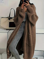 Woman wearing a long oversized brown ribbed knit cardigan with patch pockets, open front, over jeans