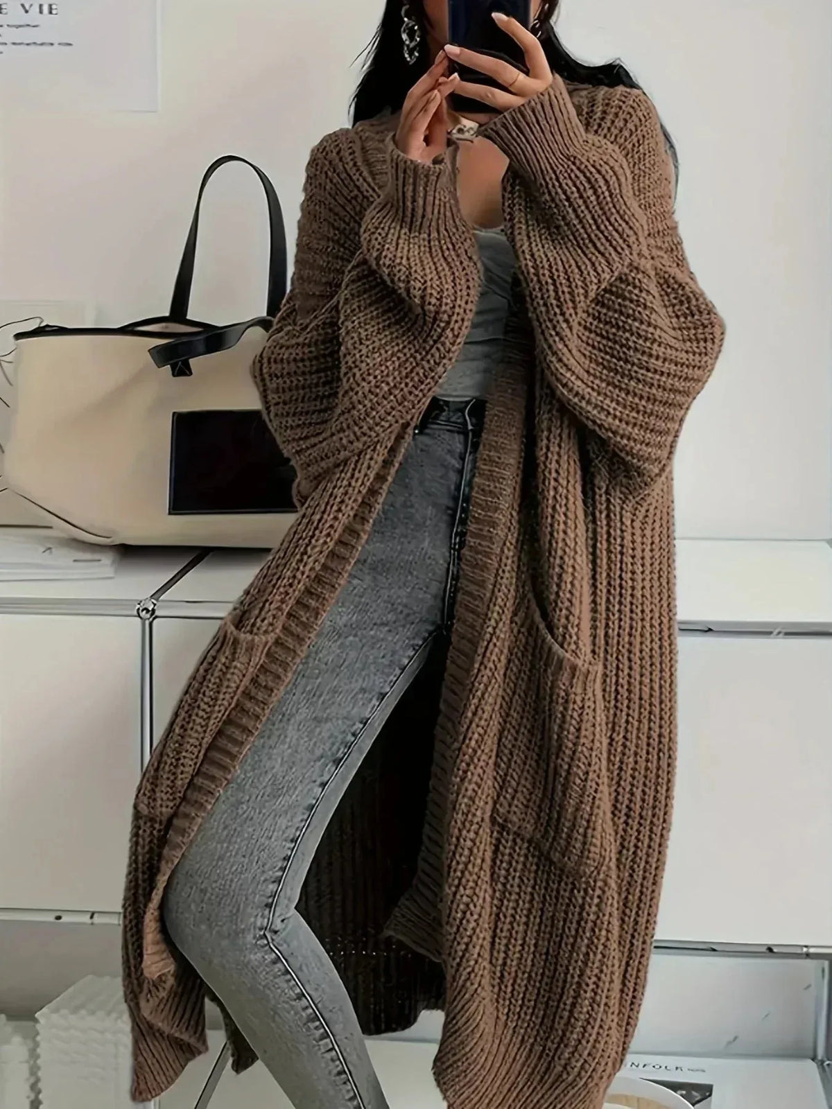 Woman wearing a long oversized brown ribbed knit cardigan with patch pockets, open front, over jeans