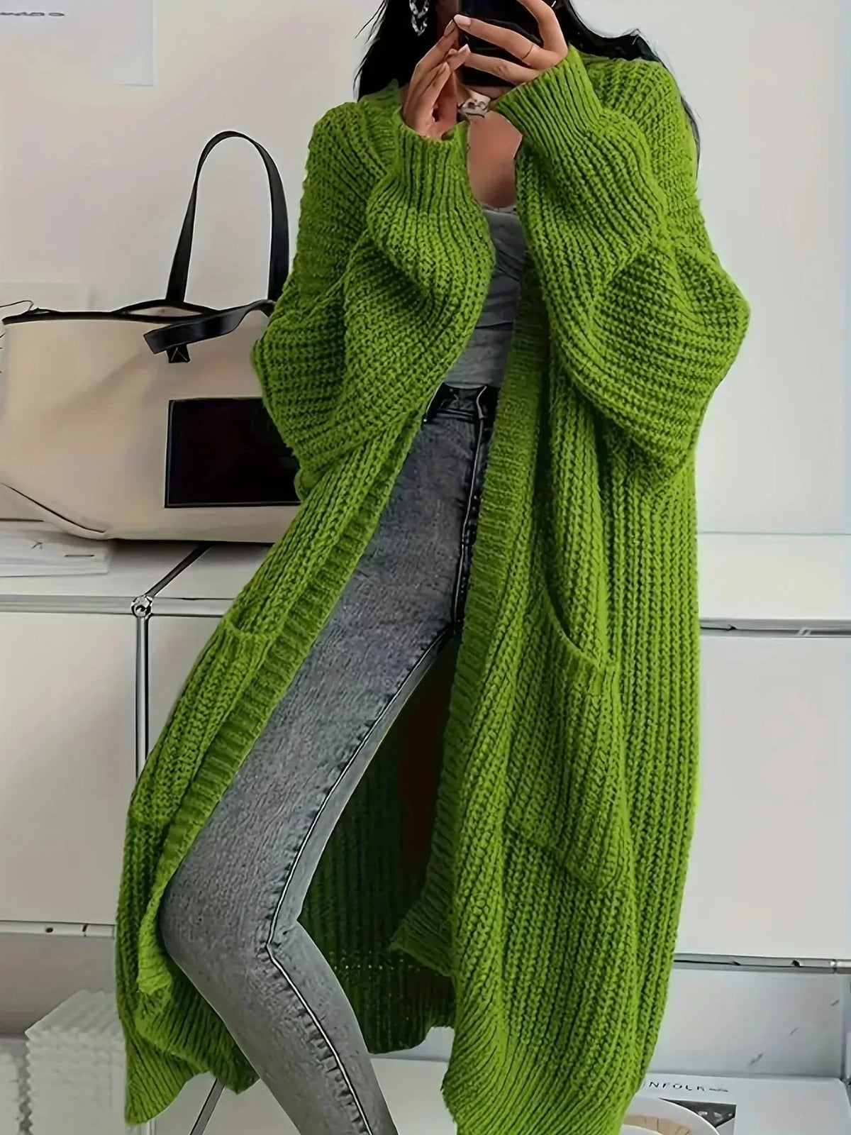 Close view of an olive green oversized chunky knit cardigan with long balloon sleeves and front pockets