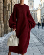 Close view of a wine red chunky ribbed knit maxi dress with balloon sleeves and tapered cuffs on a cobbled street