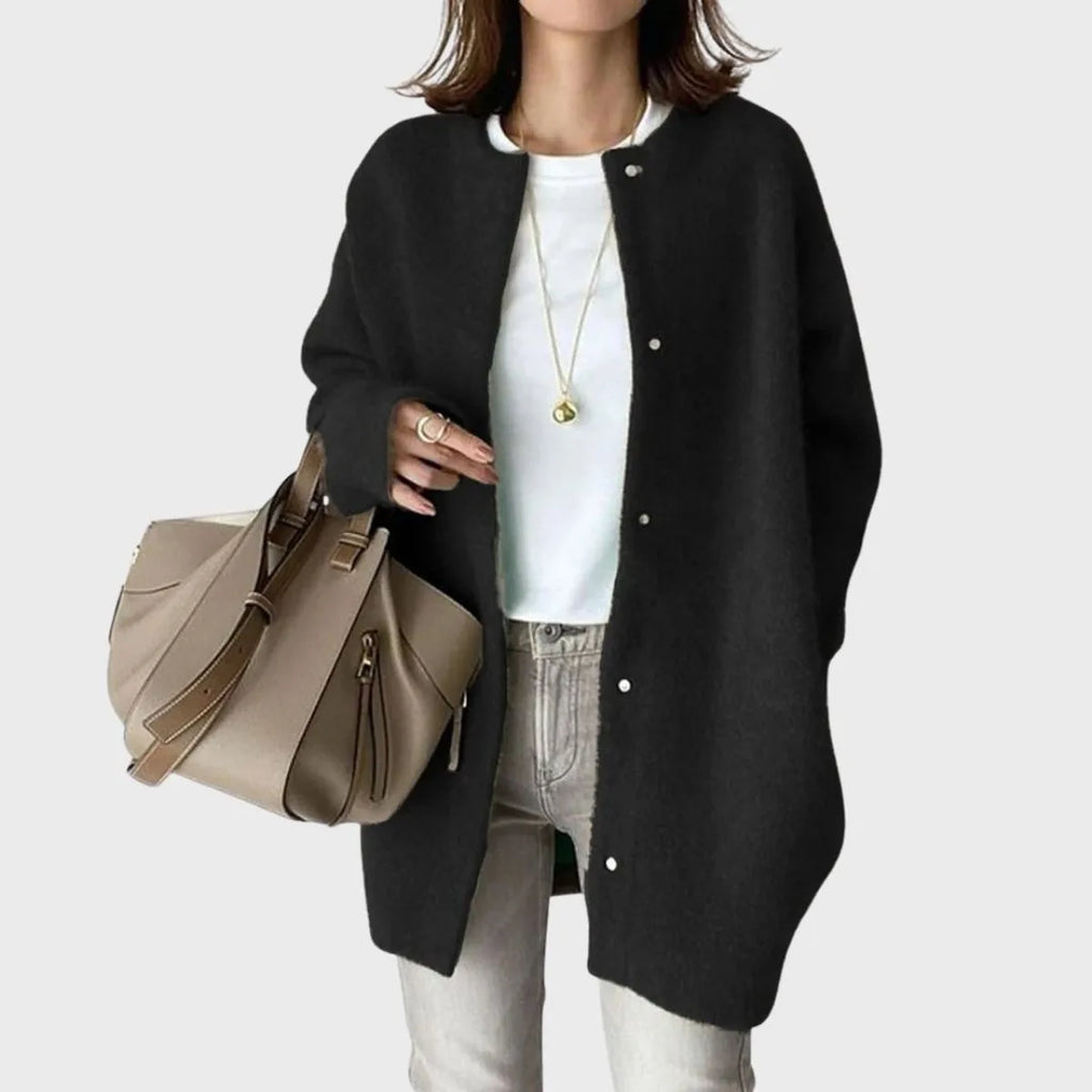 Close-up of a black oversized knit cardigan with silver snap buttons worn open over a white top