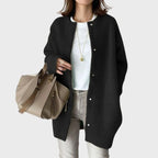 Close-up of a black oversized knit cardigan with silver snap buttons worn open over a white top