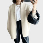Cream knit cardigan with stand collar and snap closure, worn open while holding a phone and woven leather bag