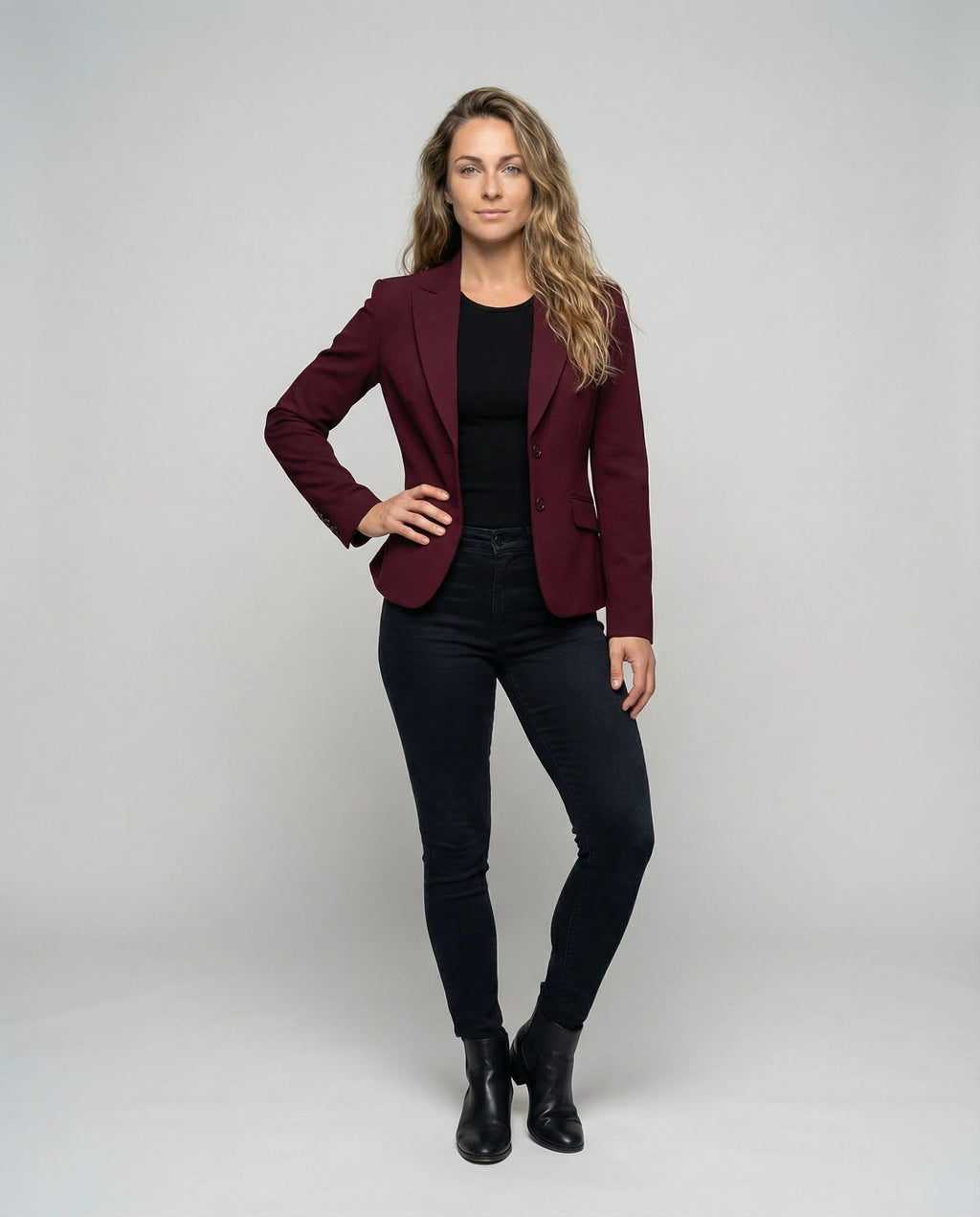 Model wearing a burgundy peplum blazer over a black top with dark jeans and ankle boots, full length front view