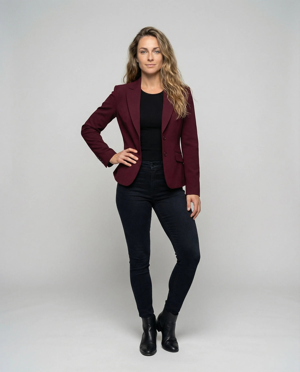 Model wearing a burgundy peplum blazer over a black top with dark jeans and ankle boots, full length front view
