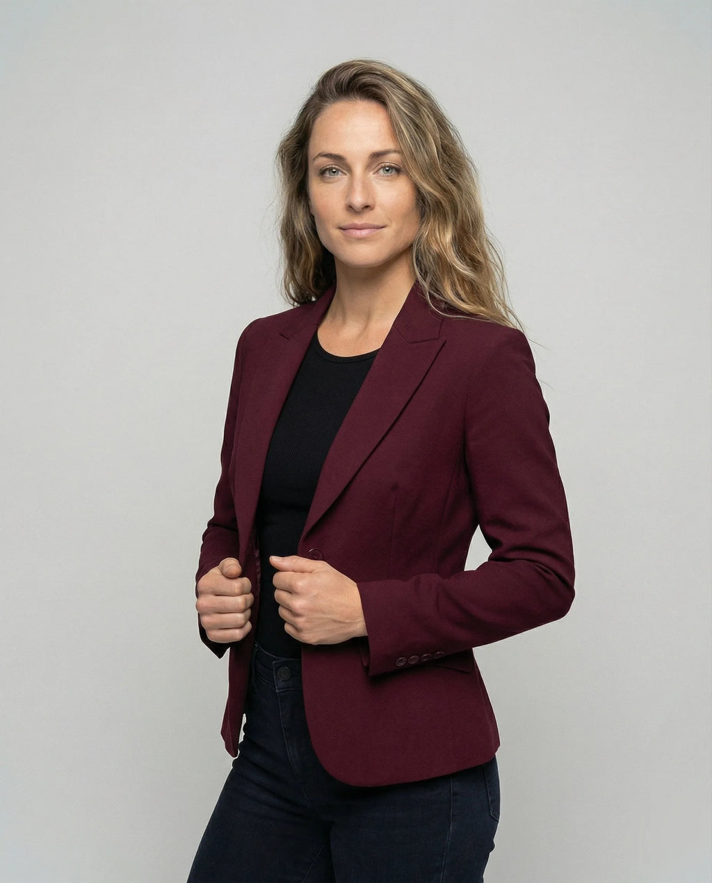 Model wearing a burgundy peplum blazer open at the front, hands holding the lapels, three-quarter view