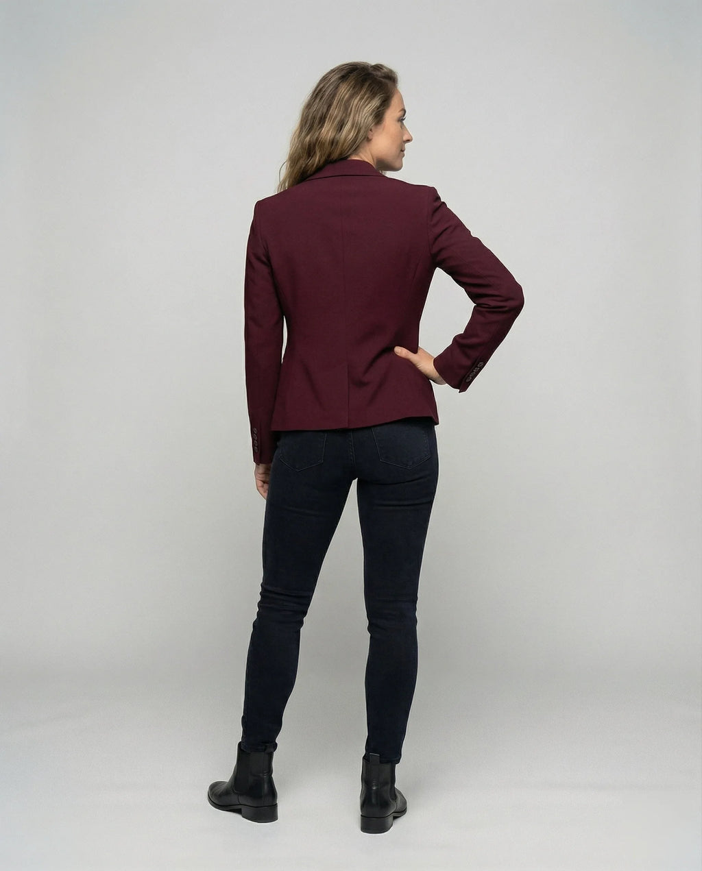 Back view of a model wearing a burgundy peplum blazer, showing the fitted waist seam and hem shape
