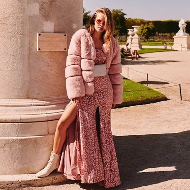 Woman in a pink faux fur puffer jacket layered over a matching pink lace maxi dress and white boots