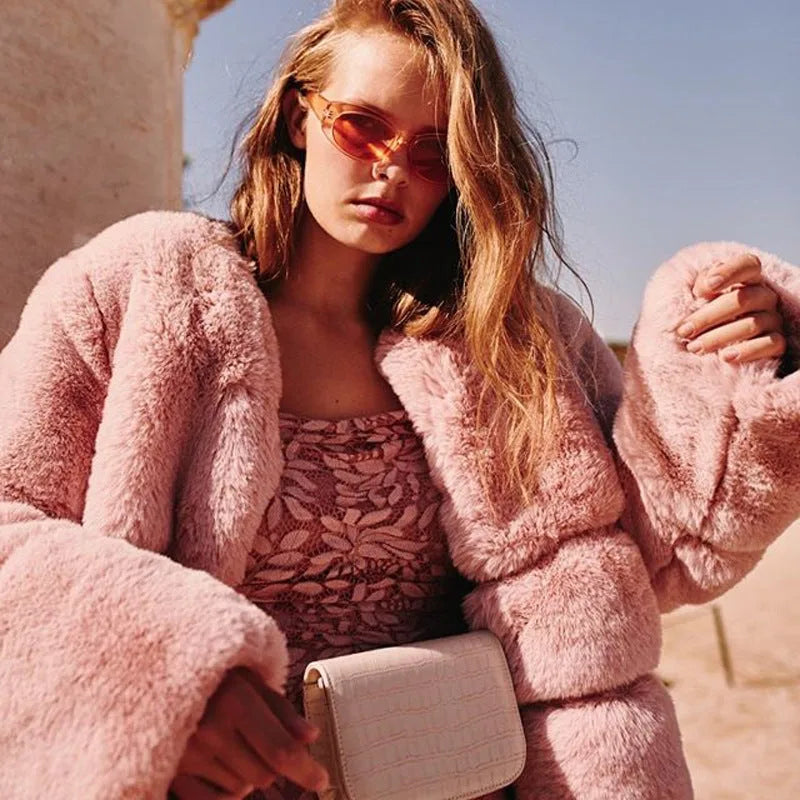 Front view of a pink faux fur puffer jacket worn open over a lace slip dress with sunglasses and a cross-body bag