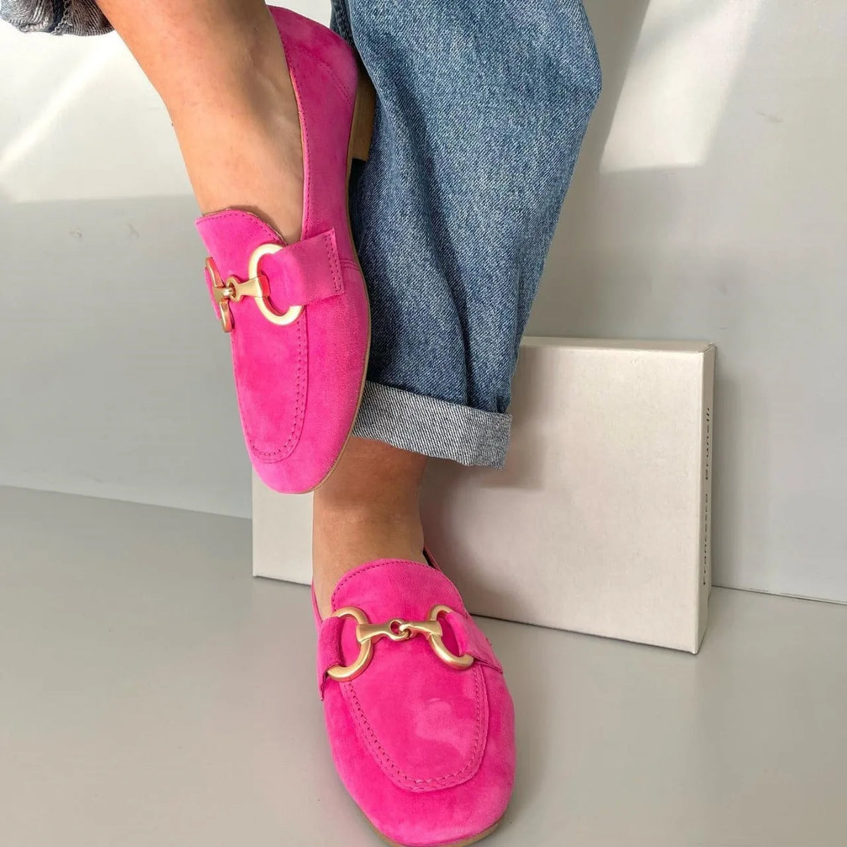 Close-up of a model wearing vibrant pink suede loafers with gold horsebit detail, styled with rolled-up jeans.