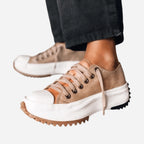 Close-up side view of tan suede platform trainers with cream toe caps and chunky treaded soles, worn with black trousers
