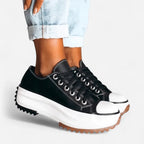 Close-up of black platform trainers with white toe caps and contrast stitching, paired with cuffed light denim jeans