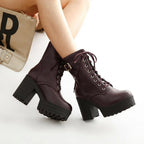 Model wearing burgundy lace-up platform ankle boots crossed at the ankles beside a cream clutch bag