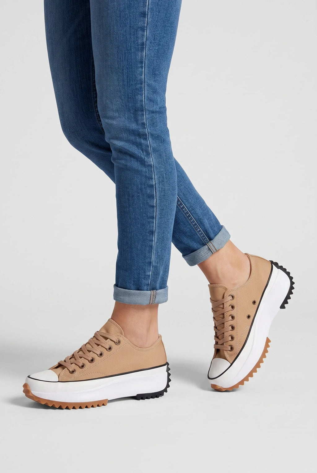 Model wearing sandstone beige platform trainers with cuffed skinny jeans, close-up on ankles and laced upper