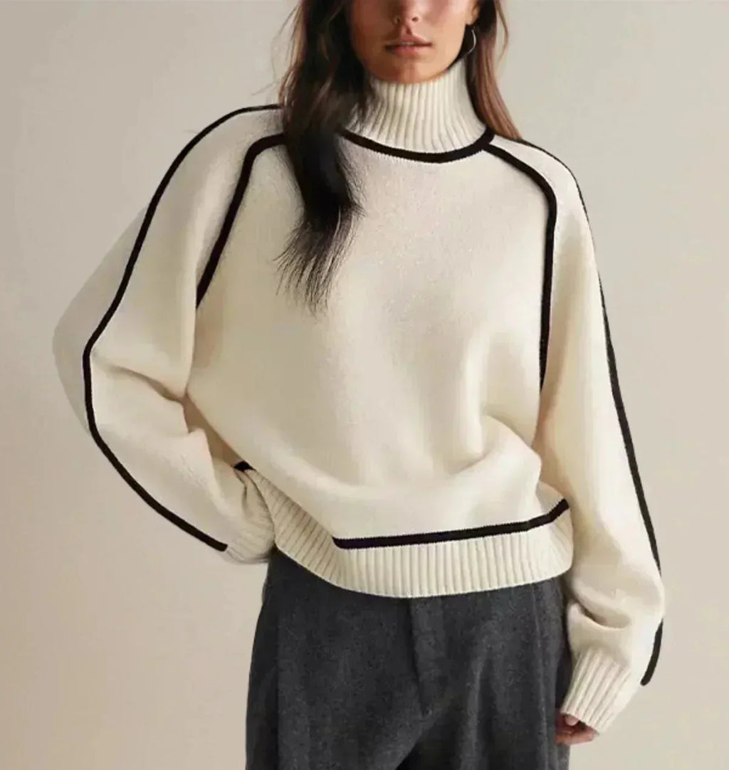 Close-up of ivory polo neck jumper with black contrast piping along raglan sleeves, worn with grey trousers