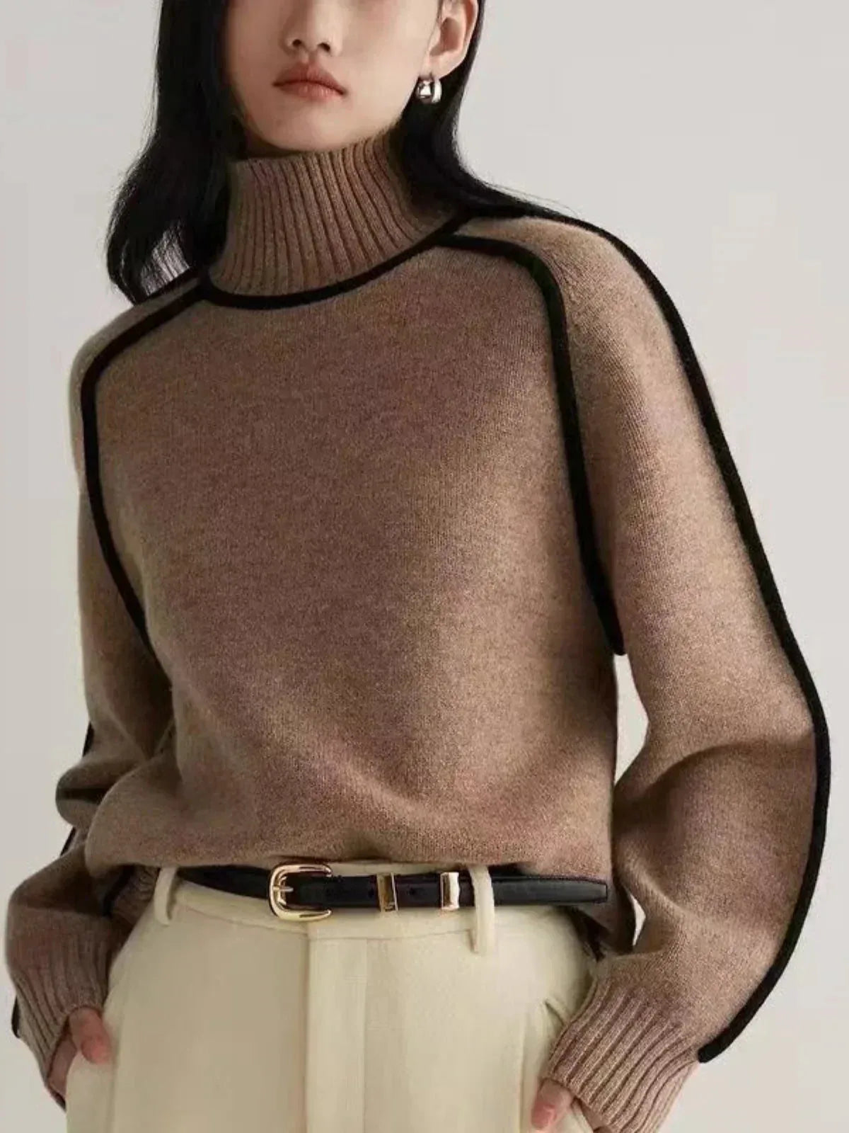 Side angle of tan knit jumper showing oversized sleeves and black contrast seam detailing