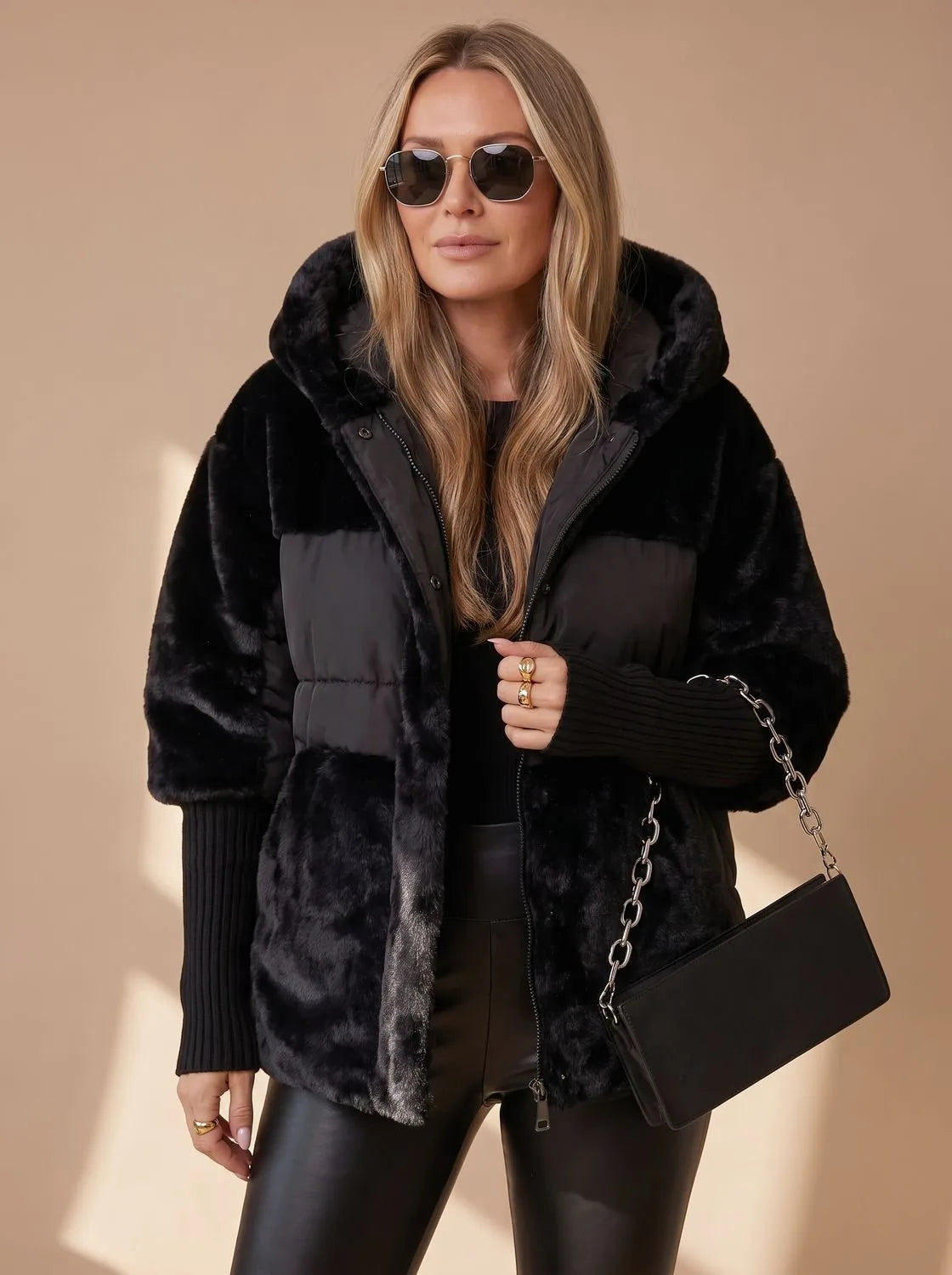 Close-up front view of black faux fur hooded puffer jacket worn with sunglasses and chain-strap shoulder bag