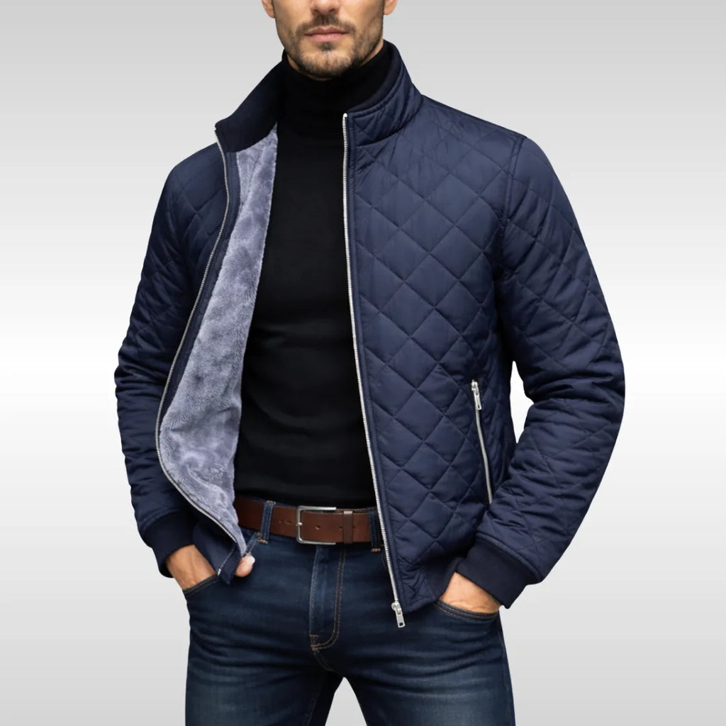 Man wearing a navy diamond-quilted jacket unzipped, revealing the soft grey fleece lining over a black polo neck